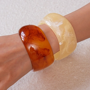 Close-up of wide resin bangles in amber sand and marble white with polished finish