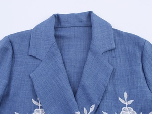 Detail view of a blue blazer showing the elegant notched lapel and white floral embroidery