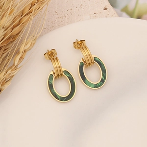 Detail view of oval geometric earrings in gold and dark green on a beige stone background