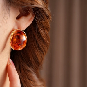 Close-up of amber resin oval earring with gold metal trim worn by a model