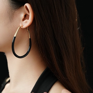 Close-up of gold and black oval hoop earrings on a model showing size and style