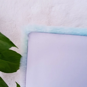 Close-up of fluffy light purple plush notebook with soft blue faux fur edge and green leaf