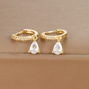 Detail of gold huggie earrings with a pear-cut cubic zirconia drop on brown texture