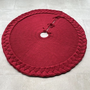 Close-up of deep red knitted Christmas tree skirt featuring cable knit texture and ties