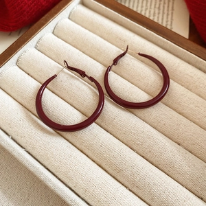 Minimalist burgundy red enamel hoop earrings displayed on a beige jewelry cushion