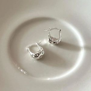 Macro shot of 925 sterling silver earrings with irregular lava texture on white plate