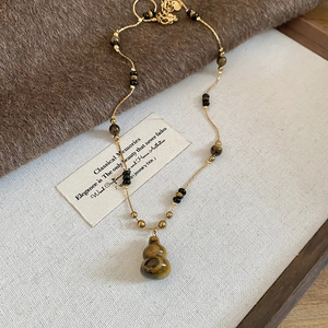 Detail of tiger eye gourd pendant necklace with gold chain on textured beige background