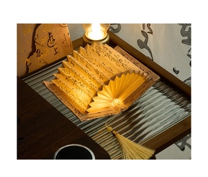Close-up of a folding fan book lamp with warm glow and traditional Chinese calligraphy