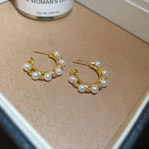 Close-up of gold plated C-shaped earrings with white pearls and small zircon stones