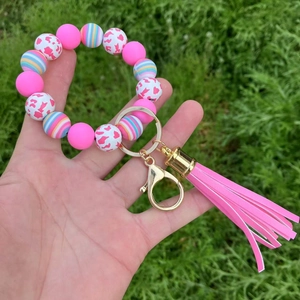Pink silicone bead bracelet keychain with gold clasp and leather tassel on grass