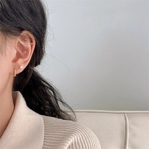 Close-up of gold twist hoop earrings paired with minimalist pearl and ball studs on ear