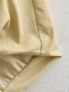 Détail macro du gilet beige montrant les coutures fines et l'ourlet plissé précis