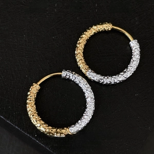 Macro detail of gold and silver mixed-metal earrings with a hammered texture on leather