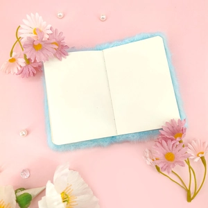 Detailopname van blauw pluche A7-notitieboek met witte pagina's op roze bloemenachtergrond