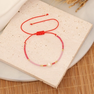 Close-up of woven seed bead bracelet with a white baroque pearl and red adjustable cord