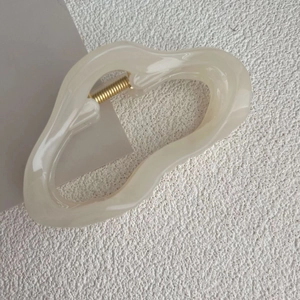 Macro detail of cream irregular hair claw clip with golden metal spring and glossy finish