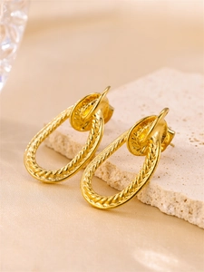 Macro shot of 18k gold plated geometric twisted earrings on stone, focus on texture