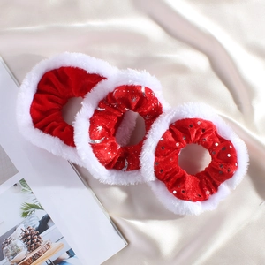 Close-up of three festive red velvet scrunchies with white fur trim and silver patterns