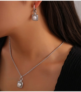 Close-up of pearl necklace and earrings set with brushed metal square pendants on model