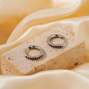 Sleek silver hoop earrings with purple zircon stones on elegant satin background
