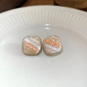 Close-up of square tweed earrings with gold edges and sparkling cubic zirconia stones