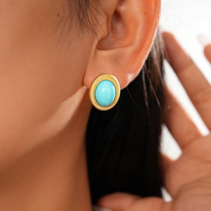 Gros plan de boucles d'oreilles dorées ovales avec pierre turquoise sur l'oreille