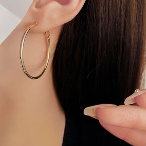 Close-up of a model wearing minimalist large golden hoop earrings with a sleek finish