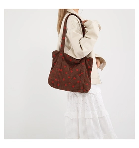Brown corduroy tote bag with red strawberry embroidery worn by a model in a beige coat