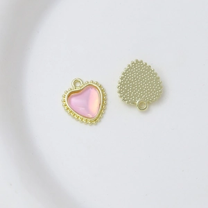 Macro view of heart-shaped gold plated pendant with pink resin stone and metal loop