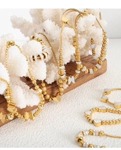 Close-up of gold beaded bracelets with butterfly and heart charms on coral decor
