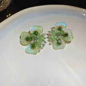 Close-up of green crystal flower stud earrings with a central pearl on ceramic background