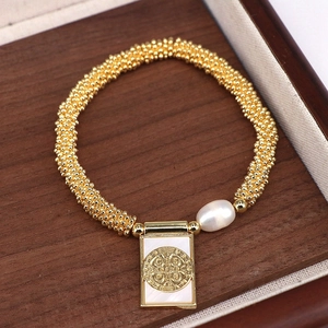 Detail of beaded gold bracelet with a natural pearl and religious St. Benedict charm