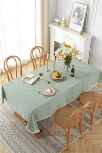 Detail of green cotton linen tablecloth featuring white decorative pom-pom fringe trim