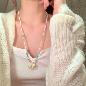 Detail view of a pearl necklace featuring a cute rocking horse pendant on a model neck