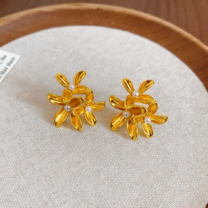 Close-up of golden vintage flower earrings with pearls on a textured beige fabric pad