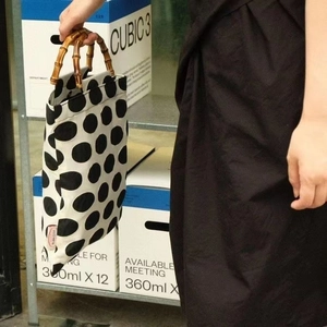 Polka dot canvas handbag with natural bamboo handles shown in a modern studio setting