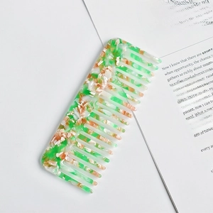 Green and pink marble acetate wide tooth comb resting on open book pages