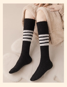 Detail von warmen Korallenvlies-Socken in Schwarz mit weißen Streifen auf Teppich