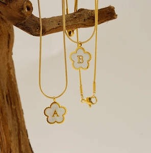 Close-up of 18K gold-plated clover necklaces with white shell letters A and B on wood