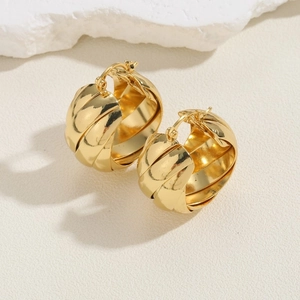 Detailed macro view of gold-tone chunky twisted hoop earrings on textured white surface