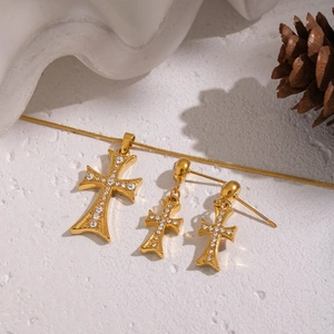 Gros plan d'un ensemble de bijoux croix dorée avec cristaux sur fond texturé blanc