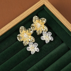 Detailed close-up of metallic flower earrings in gold and silver on dark green velvet
