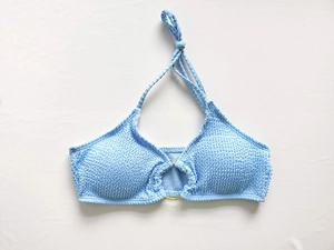 Détail du haut de bikini bleu clair texturé avec anneau doré et lanière de cou nouée