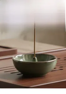 Detail of celadon ceramic incense burner with a burning stick on dark wooden tray