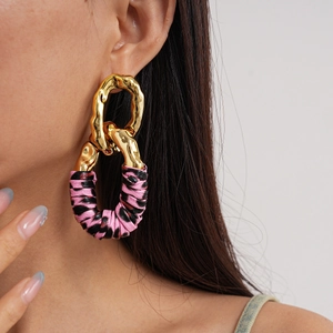Close-up of oversized gold geometric earrings featuring pink and black animal print fabric