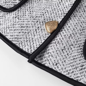 Close-up of golden textured button on tweed jacket with black piping and woven fabric