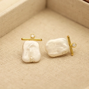 Macro shot of gold baroque pearl earrings with zircon inlay on linen texture background