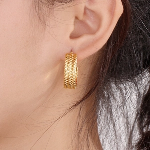Close-up of gold woven C-shape hoop earrings worn by model showing French vintage style