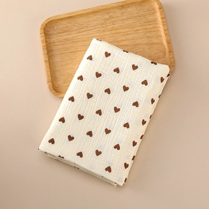 Soft muslin cotton baby swaddle blanket with brown heart patterns on a wooden tray