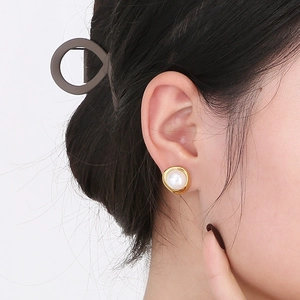 Detail of C-shaped 18K gold earrings with pearl and zircon inlay worn by model